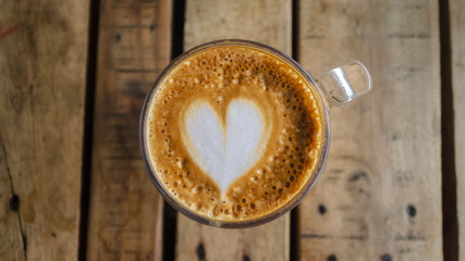 Foam with a heart for cappuccino coffee. Coffee in a transparent cup on a wooden table. View from above
