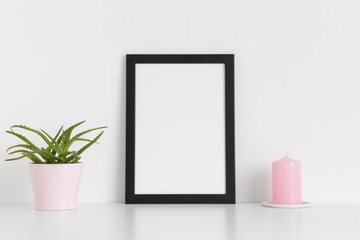 Black frame mockup with a succulent plant and a candle on a white table. Portrait orientation.