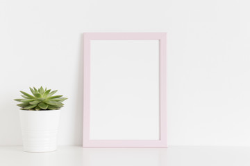 Pink frame mockup with a succulent plant in a pot on a white table. Portrait orientation.