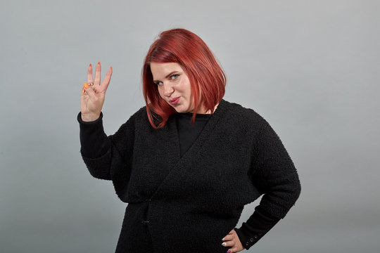 Young Redhead Fat Lady In Black Sweater On Grey Background Stylish Woman Shows Three Fingers And Smiles