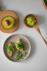 Toast with avocado, arugula on a plate and avocado or wooden board in the shape of deer antlers. Bowl with guacamole