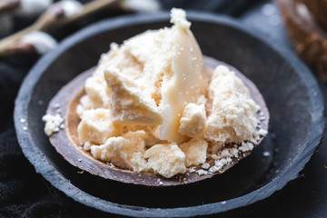 Coconut home made raw butter on a coconut bark cup on a dark table top.