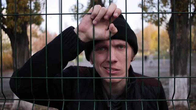 an angry man stands behind a fence. slow motion outside during the day