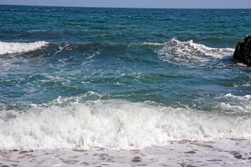 The frothy waves of the sea break on the rocks and on the beach.