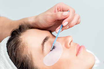 Beautiful woman receiving eyelash extension procedure, close up.