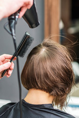 Close up of professional hairdresser is drying female hair, back view.