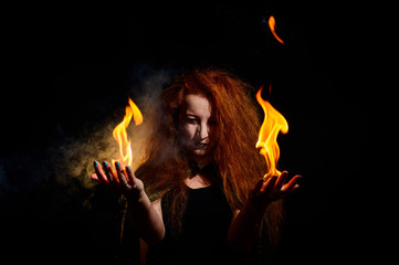 An ominous witch with long curly hair holds a magical fire. Tongues of flame on the palms of a...