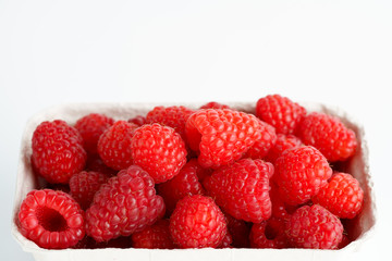 Freshly picked organic raspberries in recycled paper cup. High resolution, white background