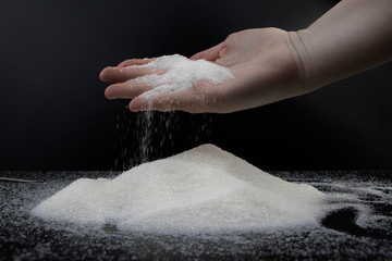 Sugar in hand on a black background. The concept of addiction to sweets. Macro photo of granulated sugar.