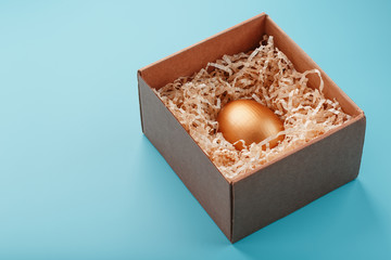 Egg made of gold in a wooden box on a blue background. The concept of exclusivity and superprize. Minimalistic composition.