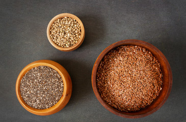 Different seeds in wooden bowls, chia, hemp, and flax top view on  dark background