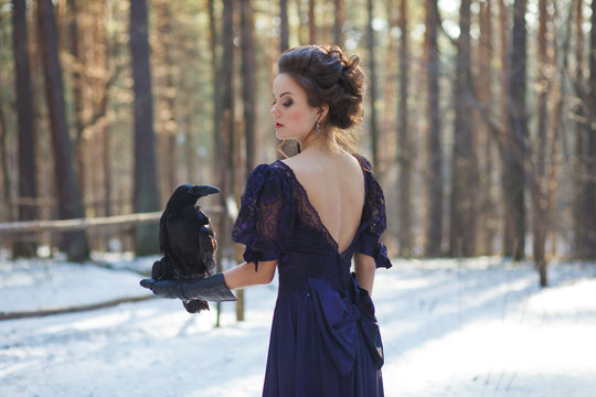 A girl walks through the winter forest with a raven in her hand.
