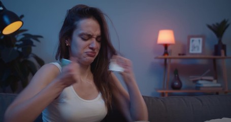 Close up of young unhappy woman tearing angrily photo and throwing away while sitting on sofa. Sad girl crying and putting hand on face after painful brokeup with lover.