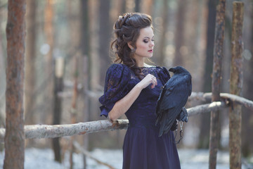 A girl walks through the winter forest with a raven in her hand.