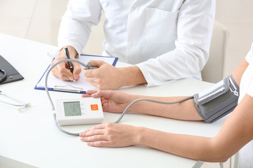 Doctor measuring blood pressure of young woman in clinic