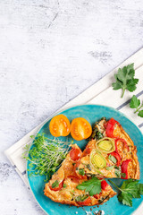 Slices of frittata with pepper, tomatoes, paprika, leek and parsley in a blue plate on a grey background, top view, copy space. Italian omelet, mediterranean cuisine, healthy breakfast, summer food.