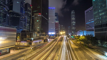 Obraz premium Hong Kong Business District timelapse at Night. Corporate building at the back and busy traffic across the main road at rush hour.