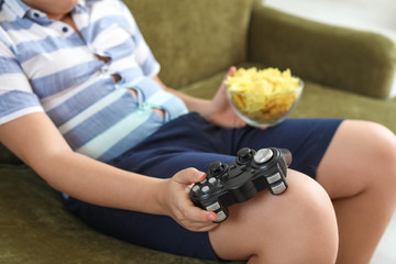 Overweight boy with chips playing video game at home