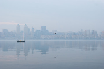 Fishing boat on the Dnieper river against the background of silhouettes of urban buildings.