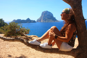 summer vacation of a brunette caucasian girl sitting on a tree branch admiring the islet of Es...