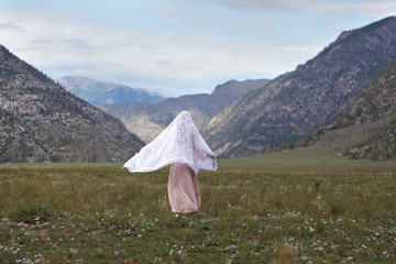 A girl walks through the meadow against the backdrop of the mountains. Prayer.