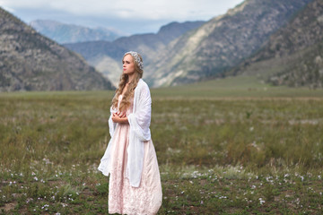 A girl walks through the meadow against the backdrop of the mountains. Prayer.