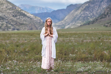 A girl walks through the meadow against the backdrop of the mountains. Prayer.