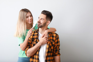 Young couple with paint brush near light wall in new apartment