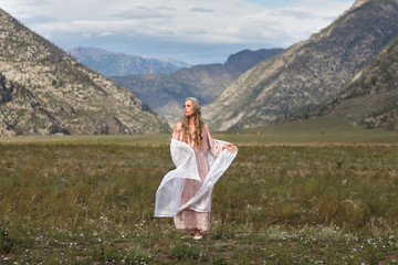 A girl walks through the meadow against the backdrop of the mountains. Prayer.