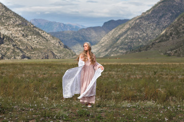 A girl walks through the meadow against the backdrop of the mountains. Prayer.