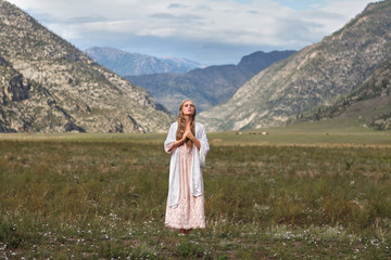 A girl walks through the meadow against the backdrop of the mountains. Prayer.