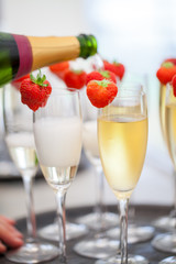 Sparkling wine or champagne and strawberry on a blurry background being poured out from the bottle during some sort of festivity or celebration such as a wedding, borthday or newyear