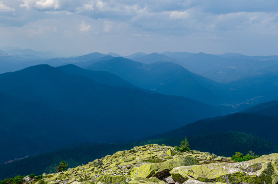 Extreme hikes. Huge stones overgrown with green ome stoch against the backdrop of high mountain ranges in the fog