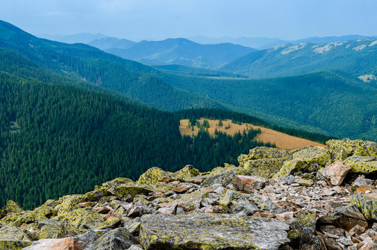 Extreme hikes. Huge stones overgrown with green ome stoch against the backdrop of high mountain ranges in the fog