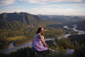 Naklejka na ściany i meble A girl in a pink dress with a long train. Bird's-eye. On the top of the mountain. Photosession in Altai