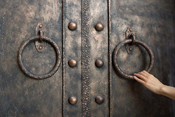 Closeup photo of elegant woman's hand holding metal ring of iron entrance door on brick wall