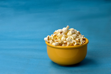delicious popcorn inside yellow bowl on blue background with space for text