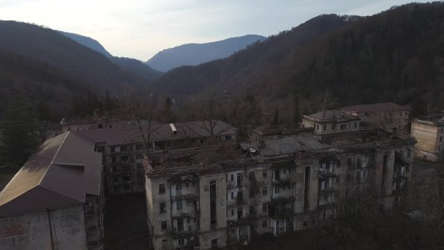 Old settlement at the top of mountain hill. Shot. Aerial view of the old abandoned residential buildings surrounded by mountains with trees.