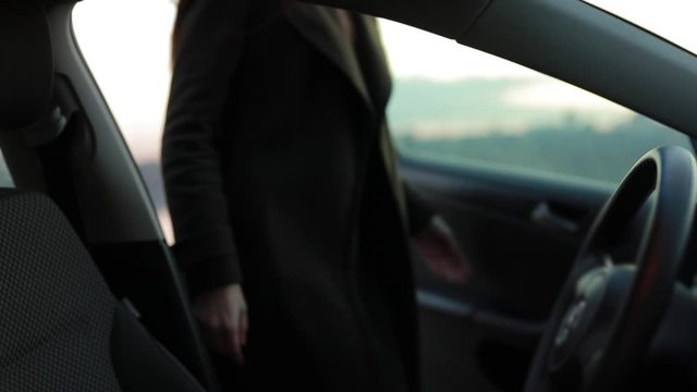 Woman sit down in her car and looking through window at the evening