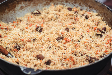 Hot pilaf in large cauldron outdoors. Tasty pilaf at street festival. Street market. Traditional oriental food. Street food concept.