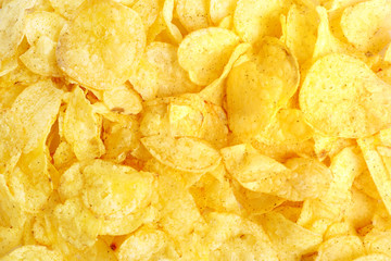 Many tasty potato chips snack background