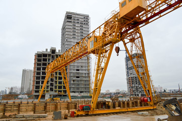 Naklejka premium High heavy yellow metal iron load-bearing construction stationary industrial powerful gantry crane of bridge type on supports for lifting cargo on a modern construction site of buildings and houses