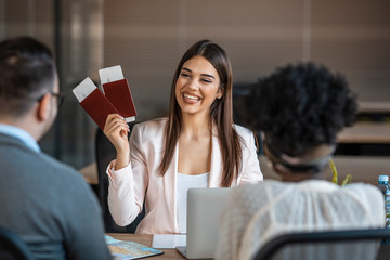Young pretty travel agent giving tickets to clients. A young man and a woman came to the travel...