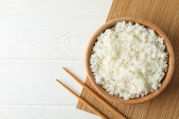 Bowl with boiled rice and chopsticks on wooden background, top view