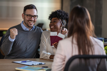 Couple sitting with manager at the travel agency office prepairing for a summer vacation. A young man and a woman came to the travel agency. They want to go on a trip during their holidays