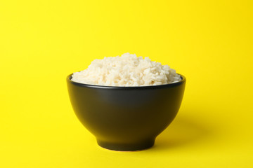 Bowl with boiled rice on yellow background, space for text