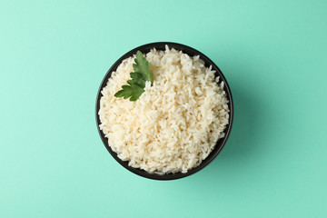 Bowl with boiled rice and parsley on mint background, top view