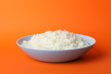 Bowl with boiled rice on orange background, space for text