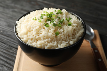 Board, bowl of delicious rice and spoon on wooden background, close up