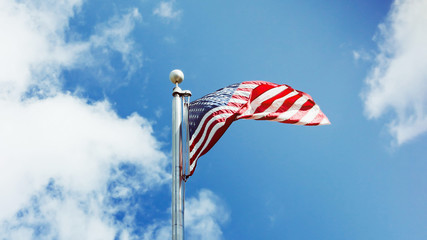 American flag against a blue sky with white clouds. 16:9 panoramic format